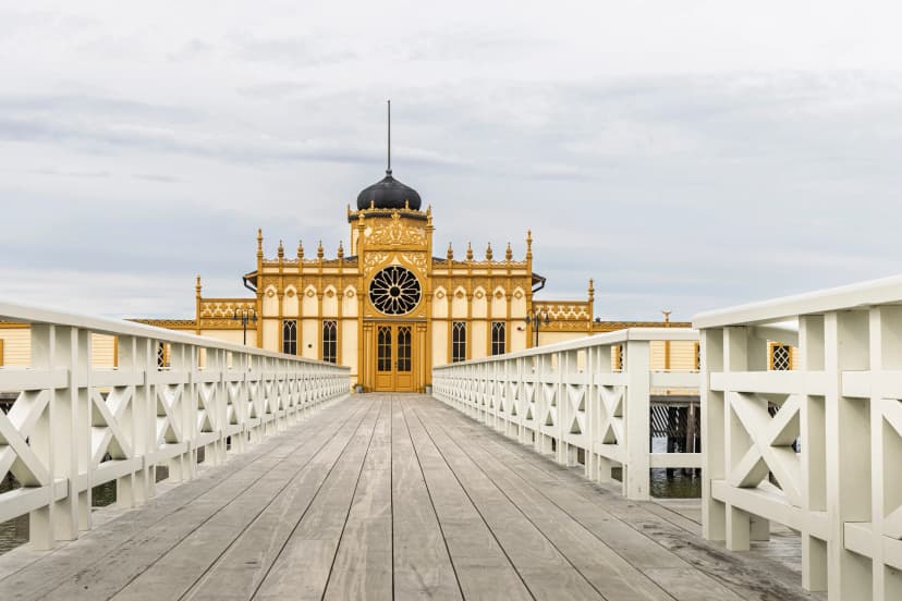 Varbergs kallbadhus on a wooden pier: ornate yellow seaside bathhouse with central rose window and white railings