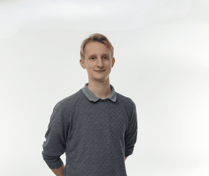 Young man wearing a grey sweater standing against a white background.