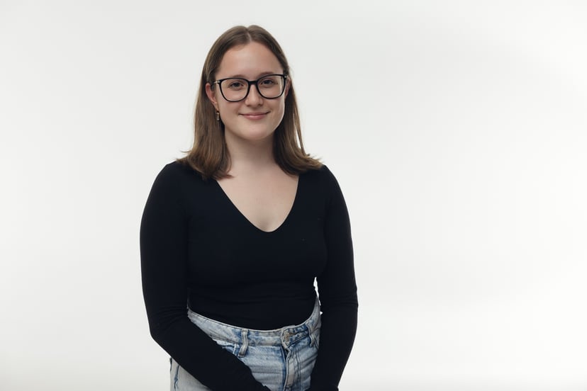 Young woman with glasses wearing a black long-sleeve shirt and jeans against a white background.