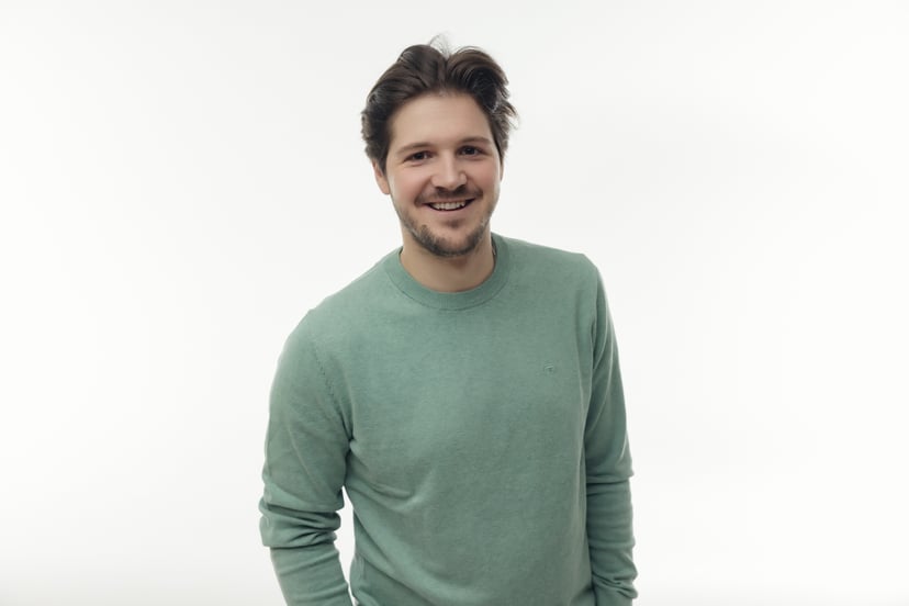 Smiling man wearing a light green sweater against a white background.