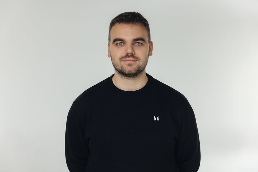 Man with short brown hair and a beard wearing a black sweater against a plain white background.