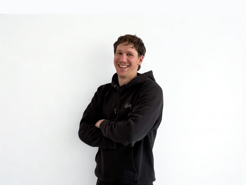 Smiling man with arms crossed wearing a black hoodie against a white background.