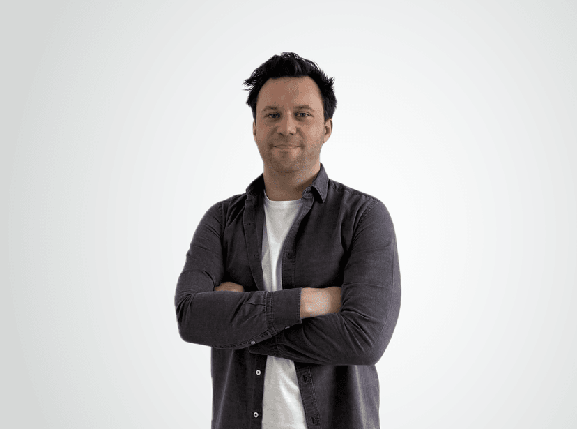 Man with arms crossed wearing a dark button-down shirt over a white t-shirt against a white background.