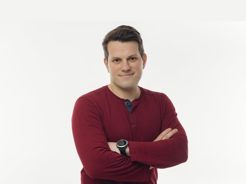 Man in a maroon long-sleeved shirt with arms crossed against a white background.